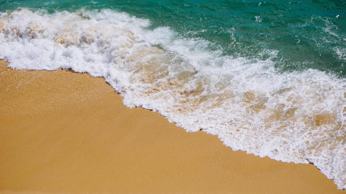 The image shows waves from the ocean crashing onto a sandy beach. 