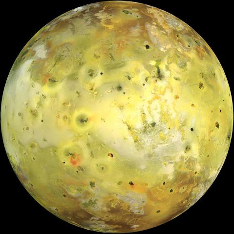 Image of Io, one of Jupiter's moons, featuring a yellowish surface dotted with dark volcanic pits, bright patches, and large areas with a range of colors from red to green, indicating active volcanic regions