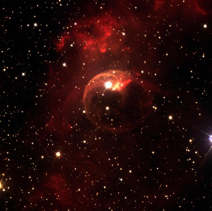 A bright red cloud against a black, starry background. The cloud is in a wispy, vertical column in the middle of the image. In front of this, part of the cloud has formed a bubble-like shape that is slightly more orange in colour.